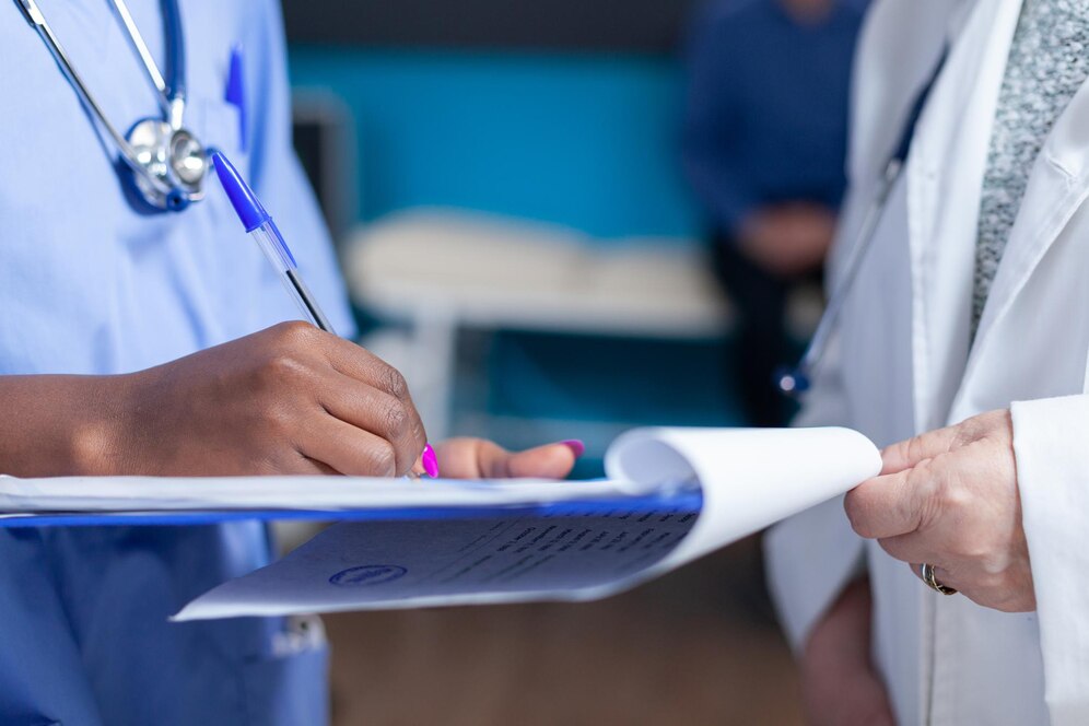 close-up-nurse-signing-files-wtih-help-from-doctor-healthcare-cabinet_482257-27149